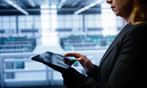 System administrator monitoring server room, doing checkup, inputting data on tablet of needed fixes. IT support employee working in data center facility housing storage rackmounts, camera B close up